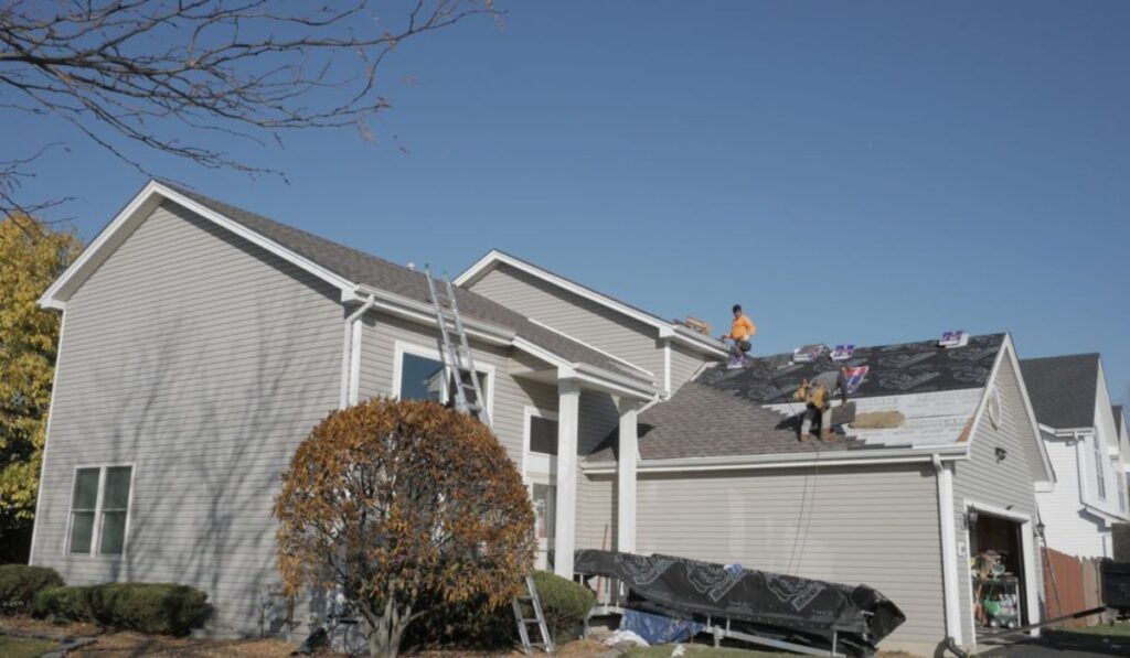 two roofing professionals on top of a roof working on roof replacement
